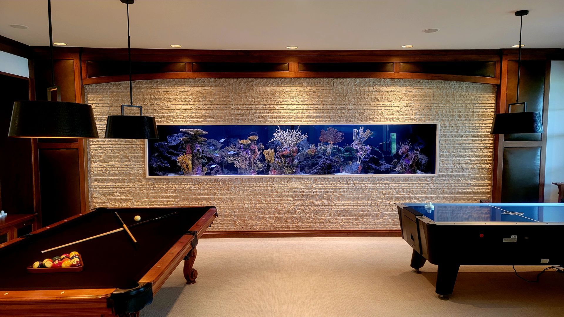 A pool table and air hockey table in a room with a large aquarium on the wall.