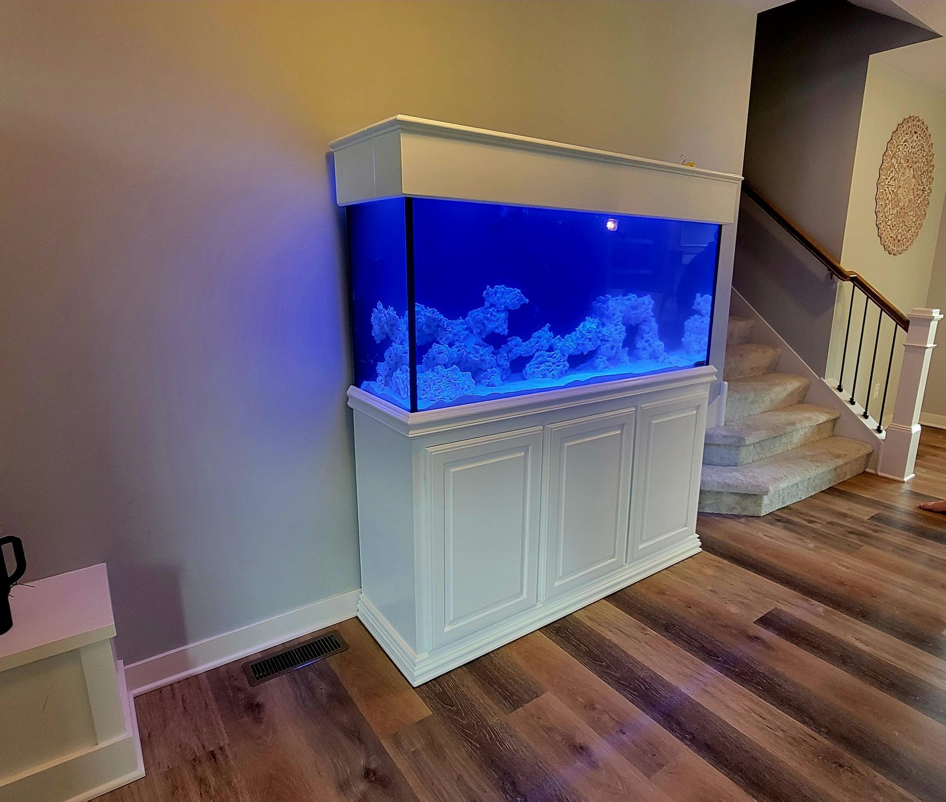 A large aquarium is sitting in a living room next to a staircase.