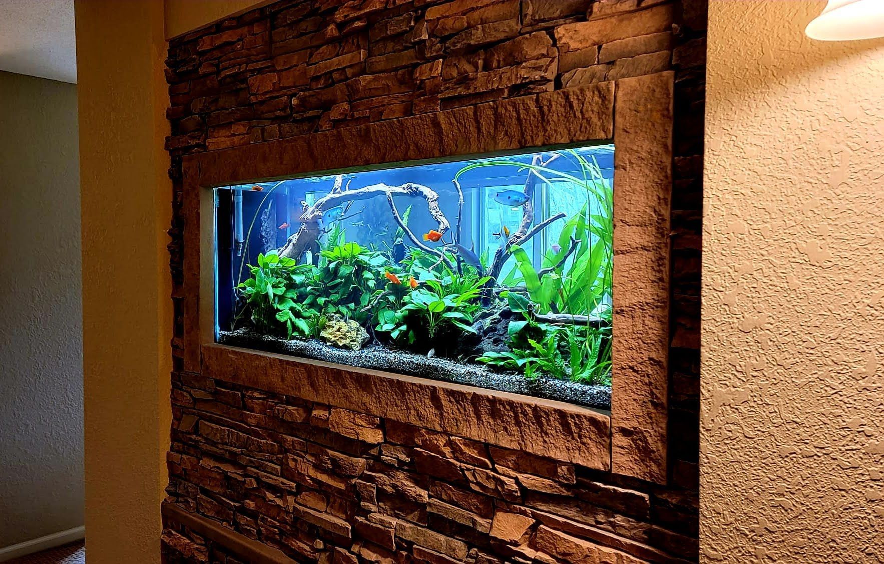 A large fish tank is hanging on a brick wall.