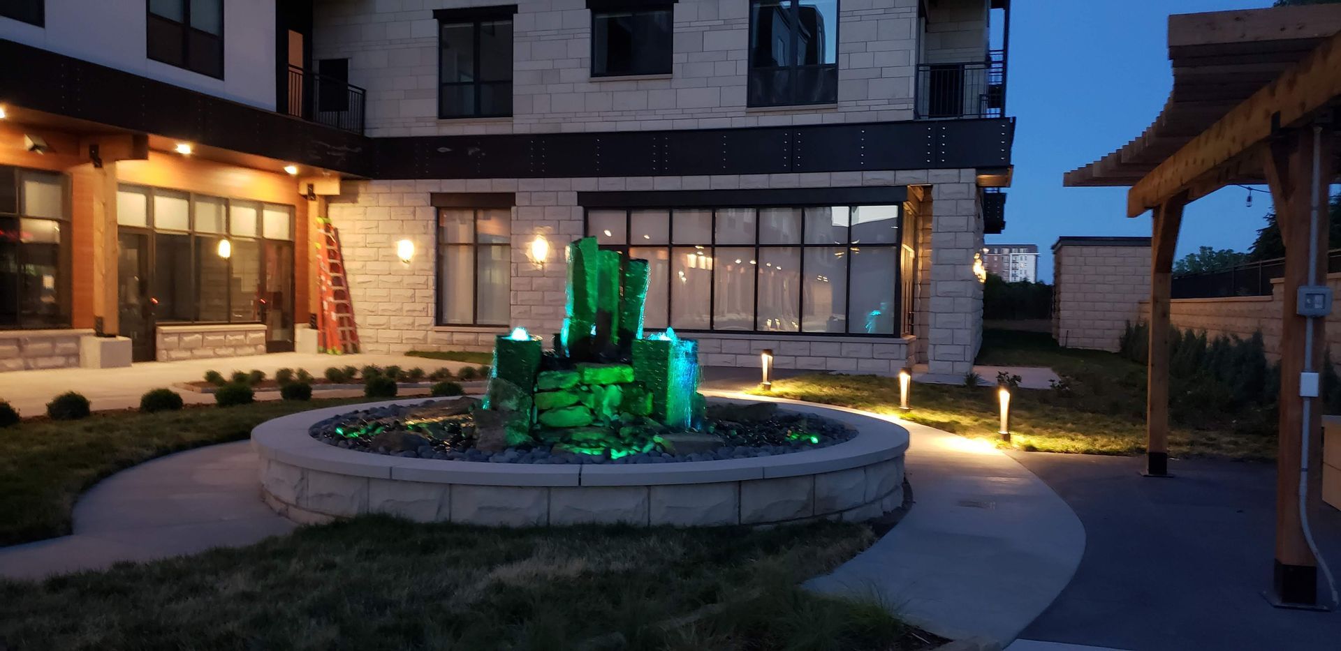A green fountain is in front of a building at night.