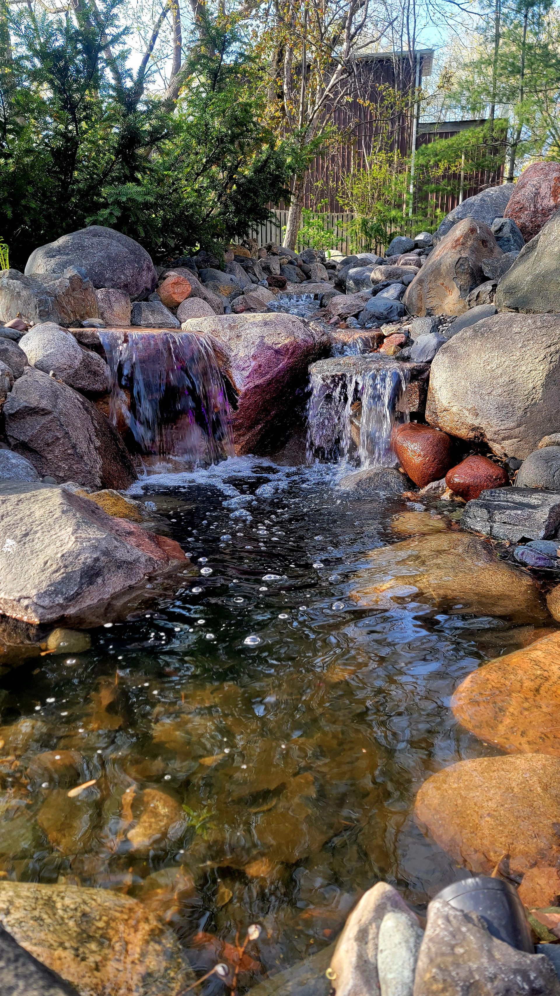 A small waterfall is surrounded by rocks and trees in a park.