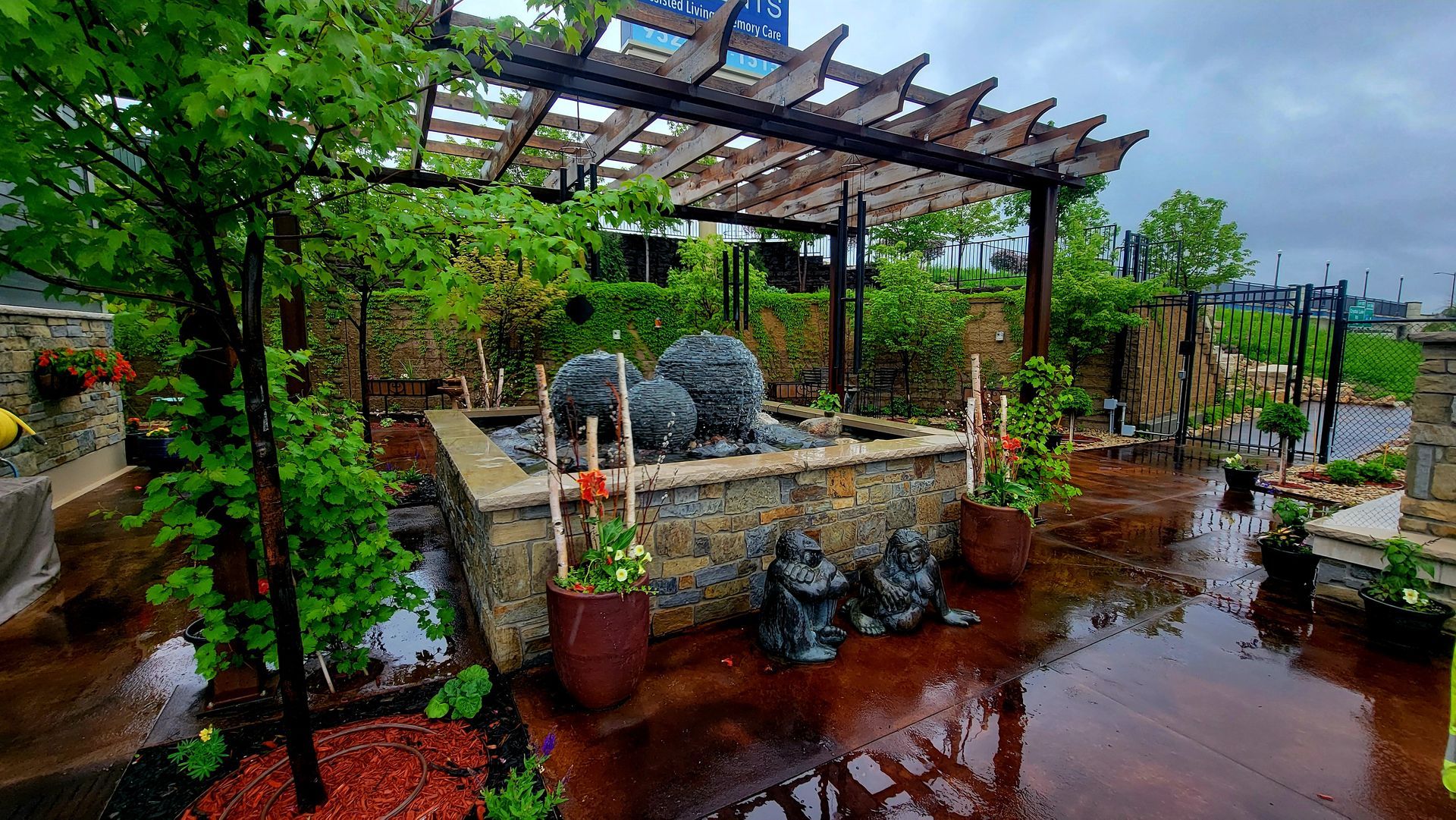 There is a fountain in the middle of the garden with a pergola over it.
