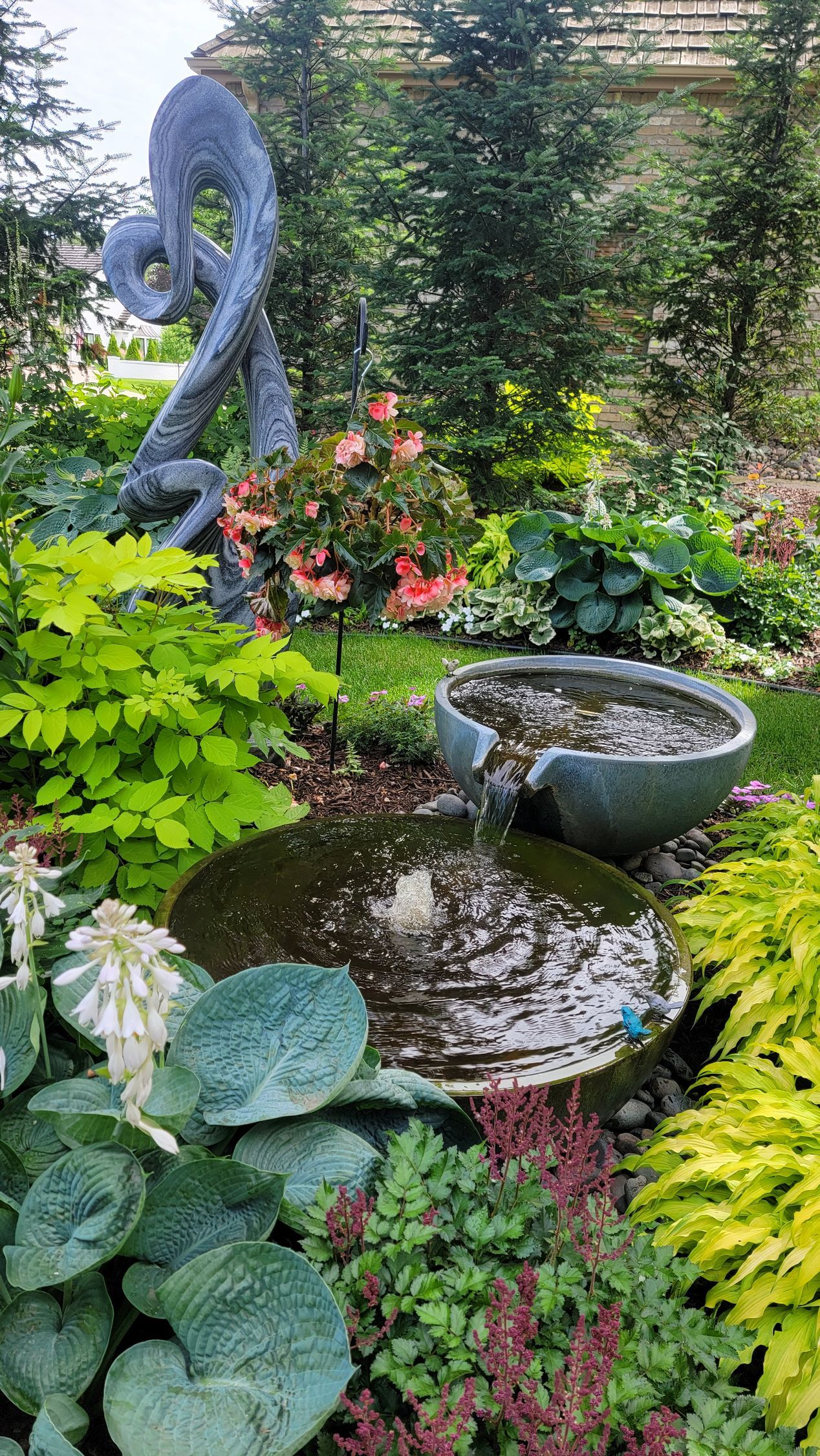 There is a fountain in the middle of the garden surrounded by plants.