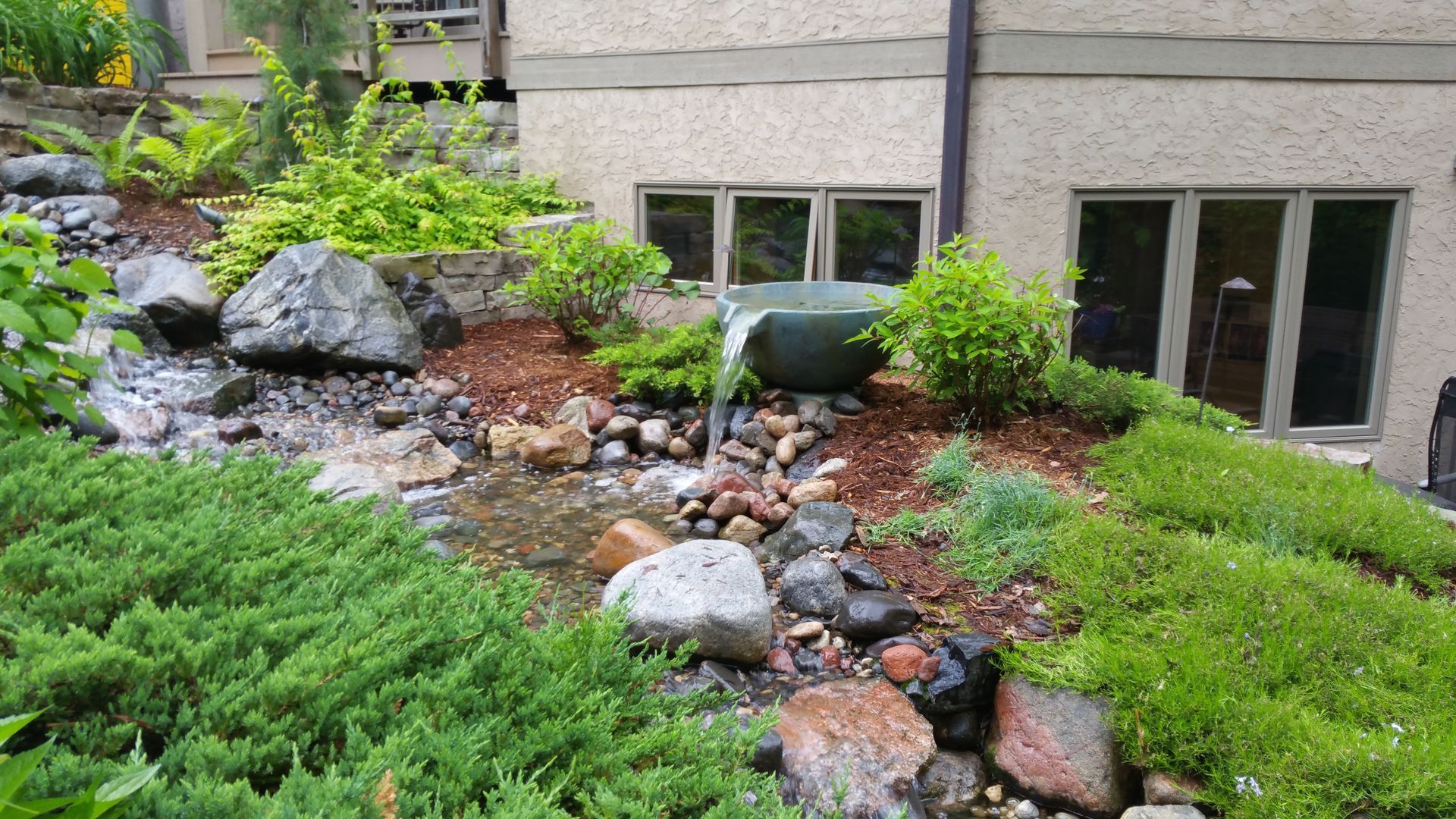 A waterfall is surrounded by rocks and plants in front of a building.