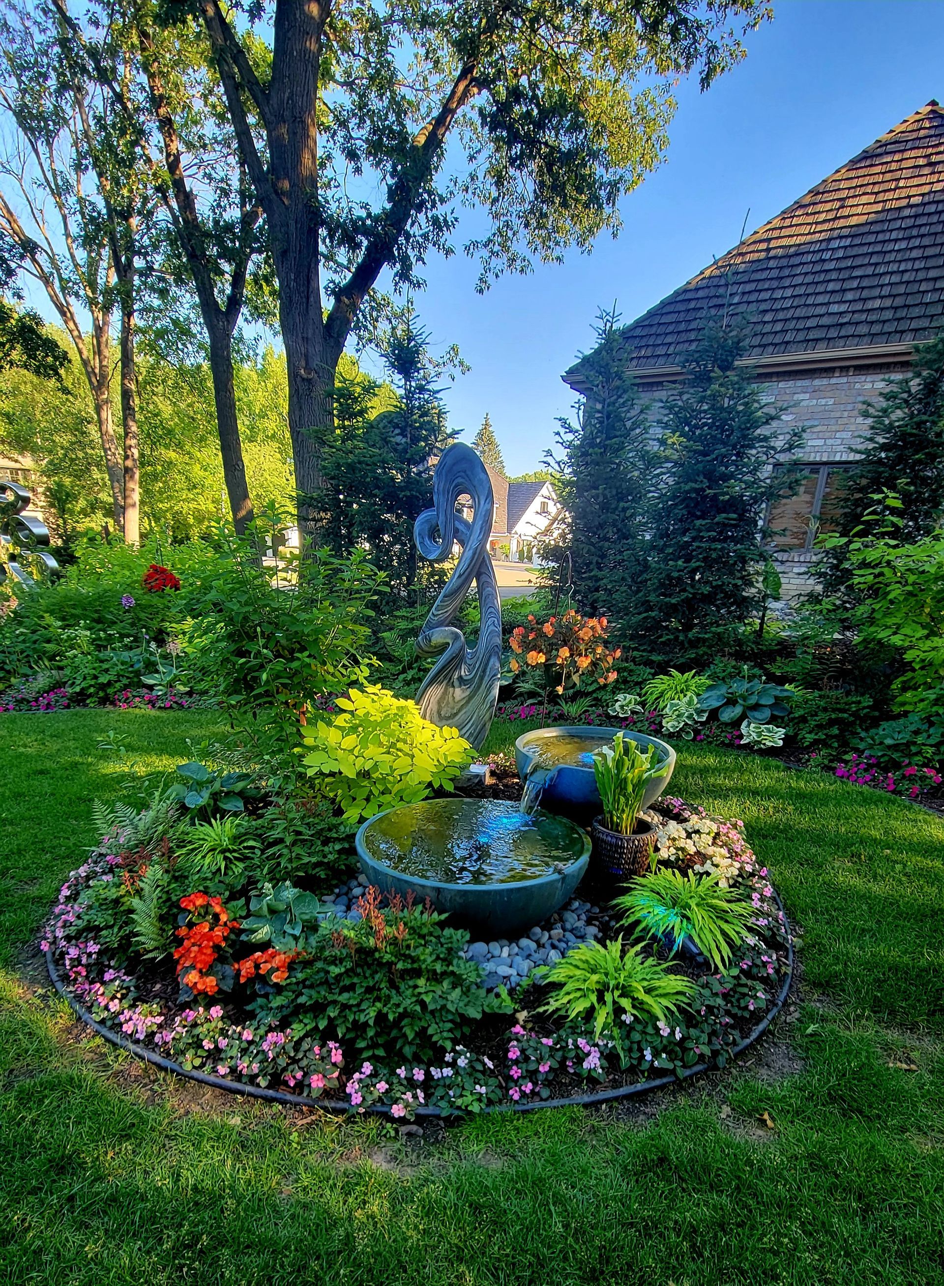 There is a fountain in the middle of the garden surrounded by flowers.