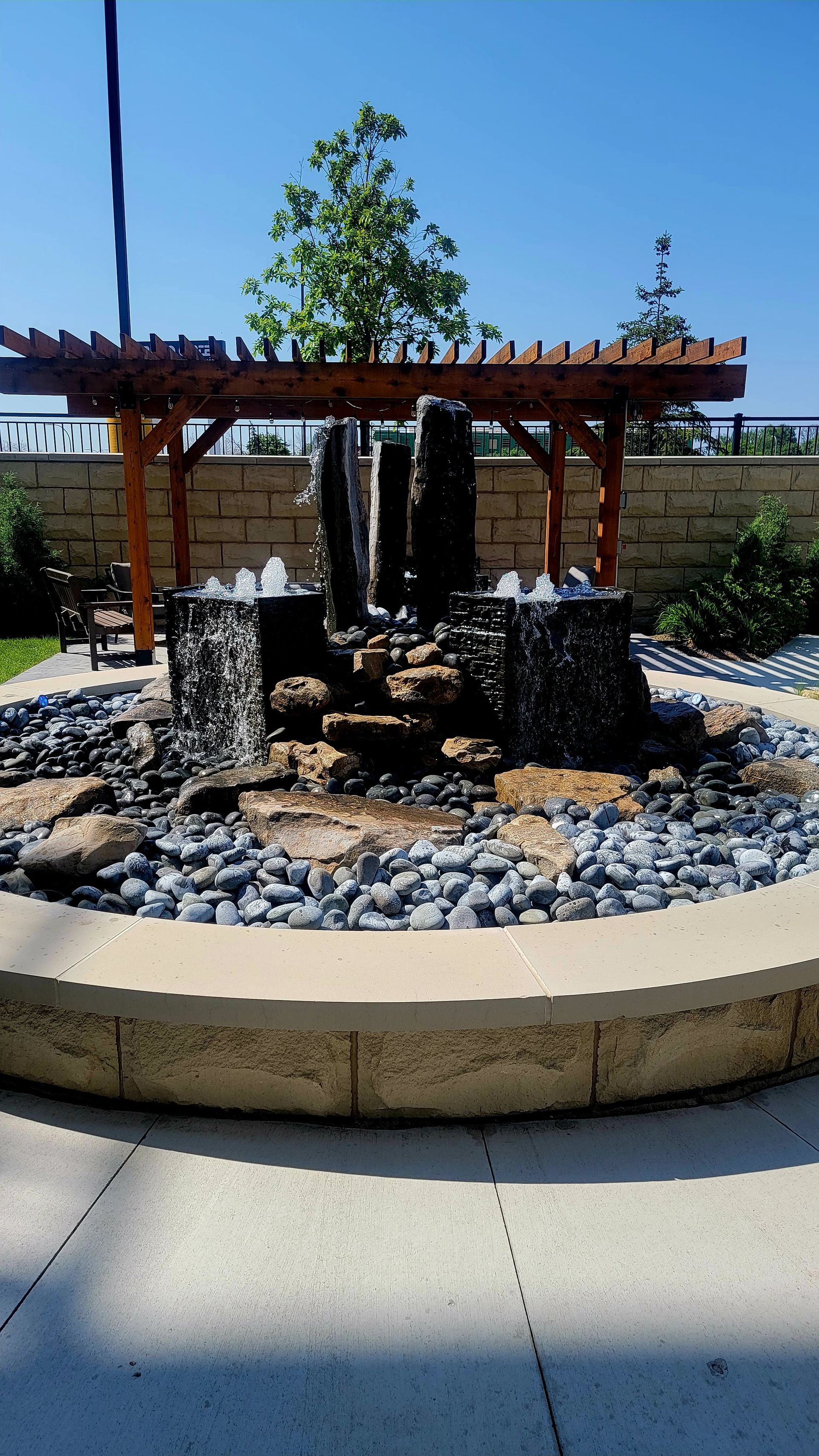 A fountain in a park with a pergola and a tree in the background.