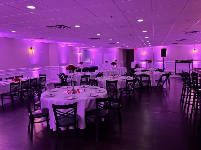 a large room with tables and chairs set up for a wedding reception with purple lighting .