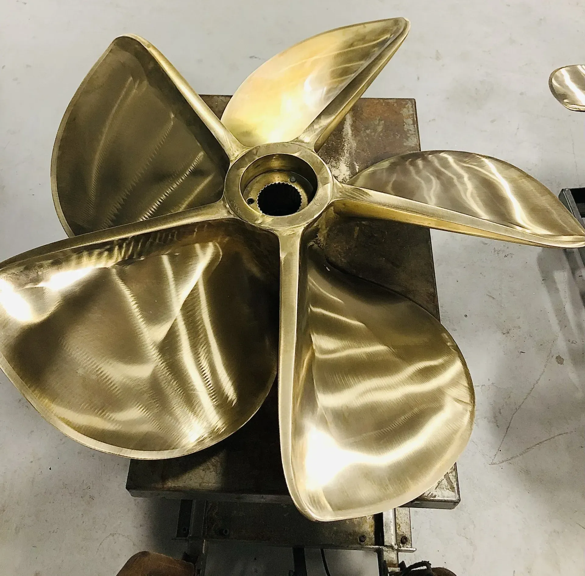 Four-bladed bronze boat propeller resting on a metal surface, with shiny blades and central hub.