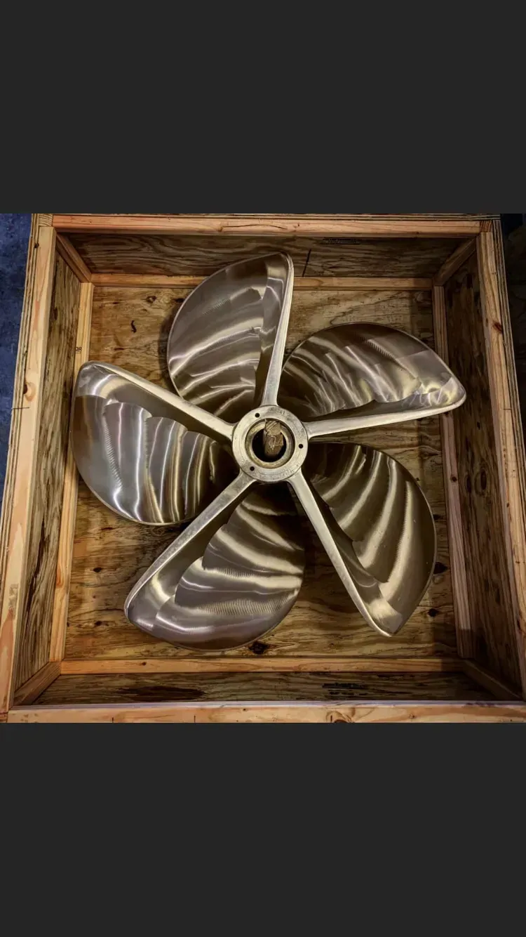 Large, shiny, five-bladed boat propeller in a wooden box.