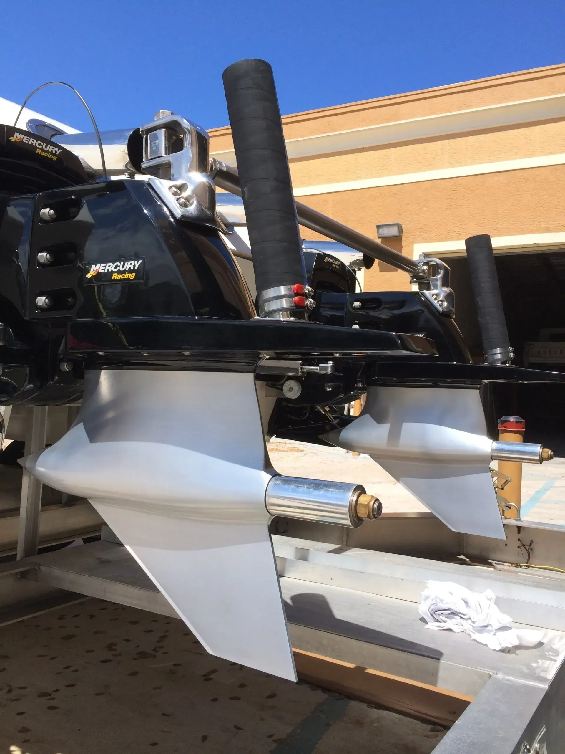 Boat propellers, shiny silver, mounted on a black engine; view is close up, outside in daylight.