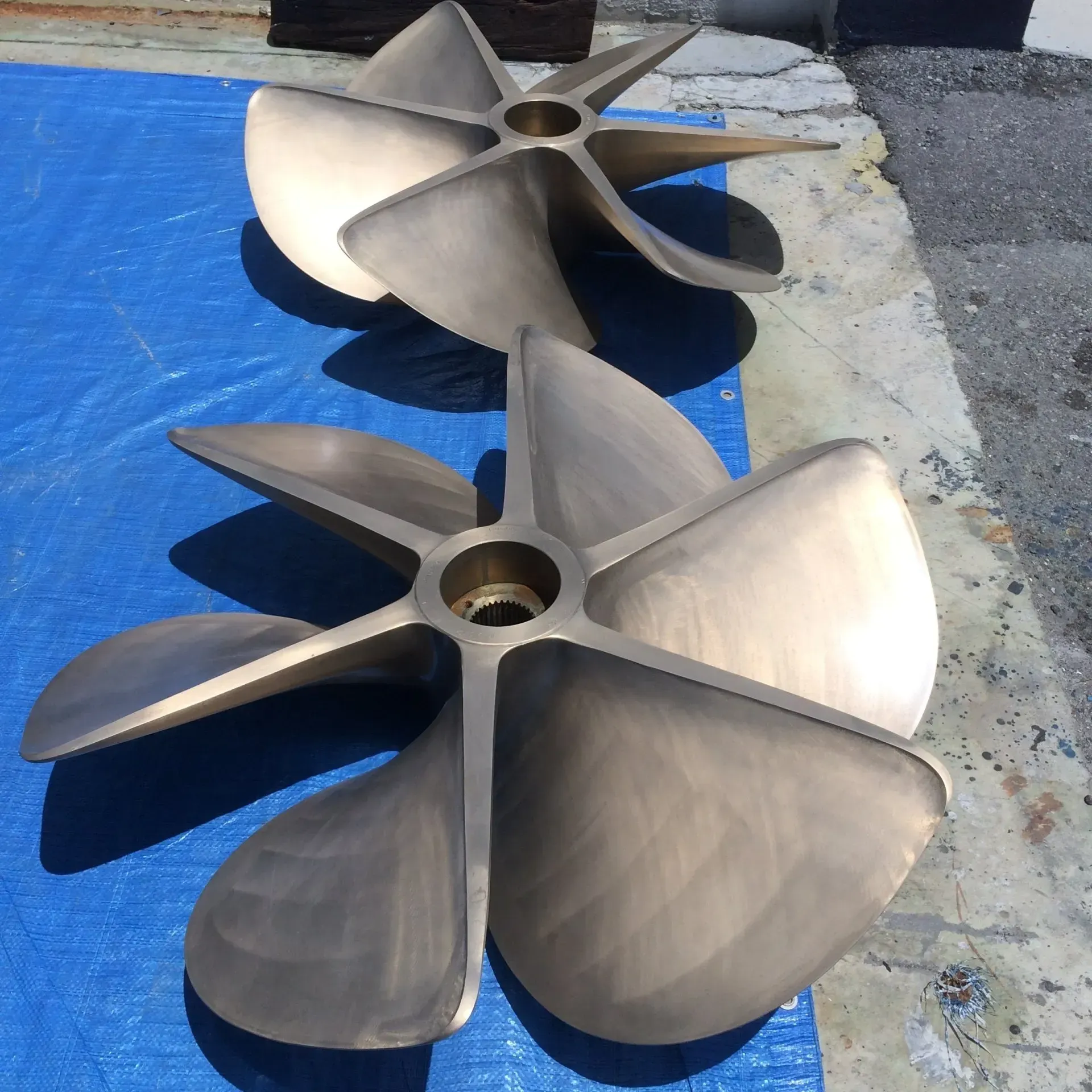 Two bronze boat propellers on a blue tarp, outdoors.