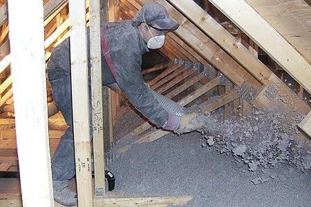 A man wearing a mask is blowing insulation into an attic