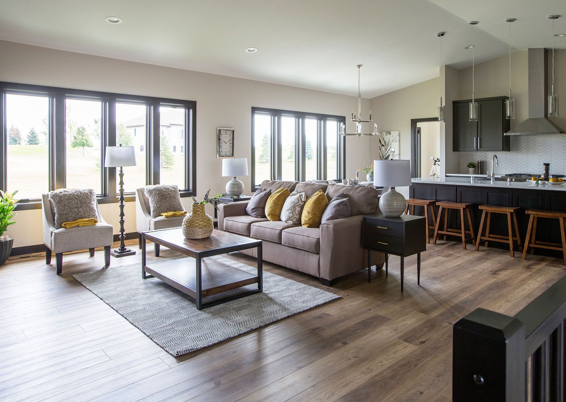 Bright open living room with gray sofa, patterned chairs, coffee table, and kitchen bar seating.