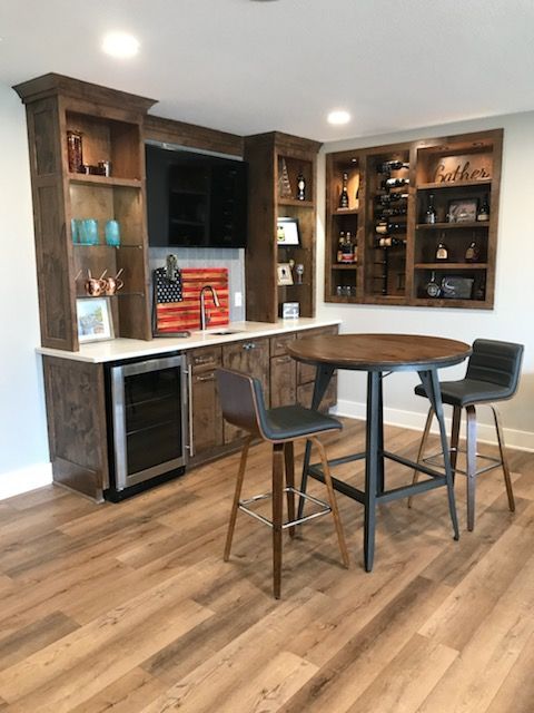 Modern kitchen bar area with built-in wooden cabinets, black stools, and wood flooring