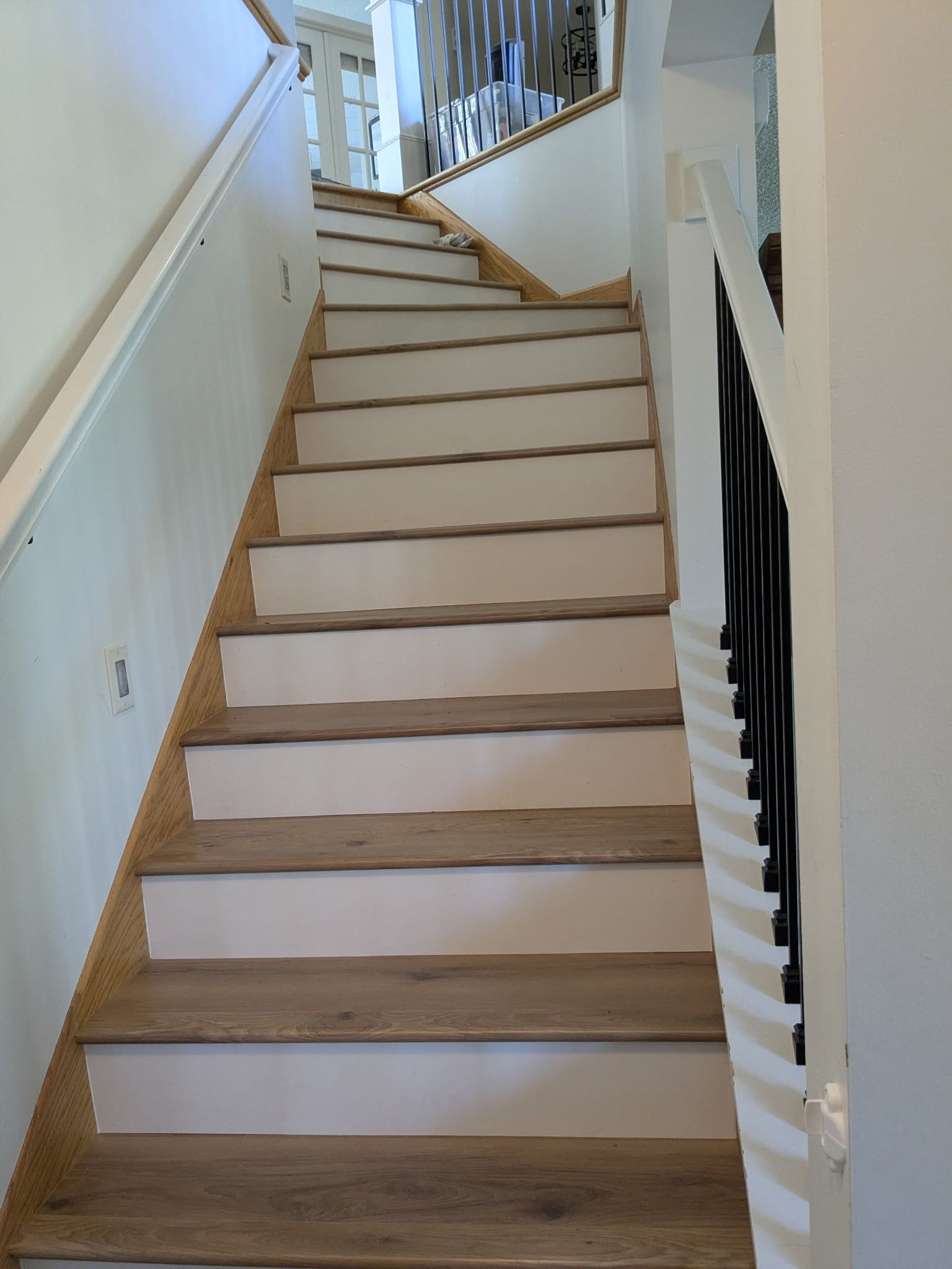 Indoor staircase with white walls, wooden steps, and white railings leading upstairs