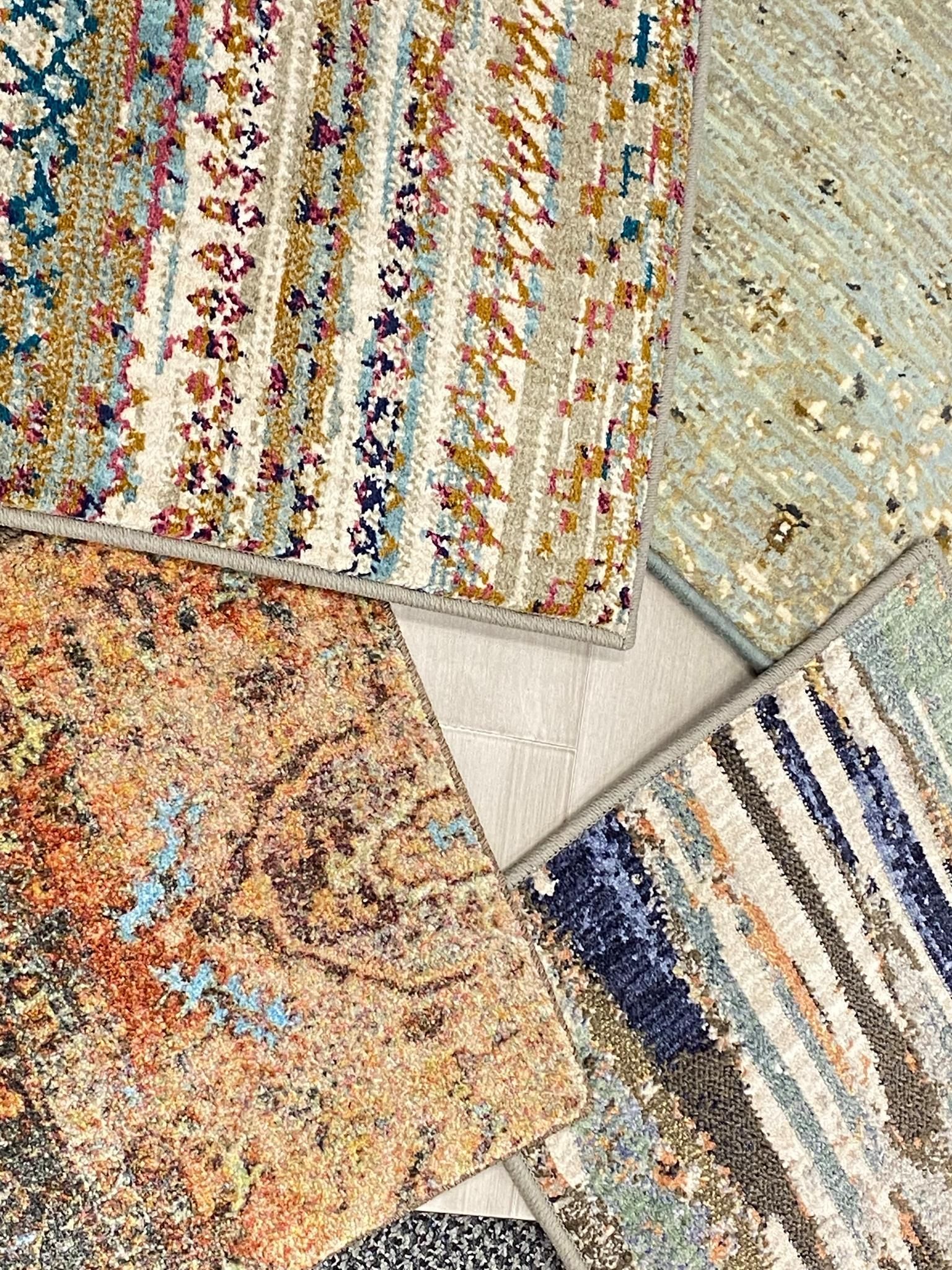 Four colorful patterned rugs overlapping on a light floor, showing textured stripes and speckled designs