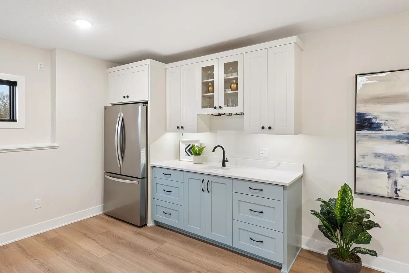 Bright modern kitchen with white cabinets, stainless fridge, light blue lower cabinets, and wood floors.
