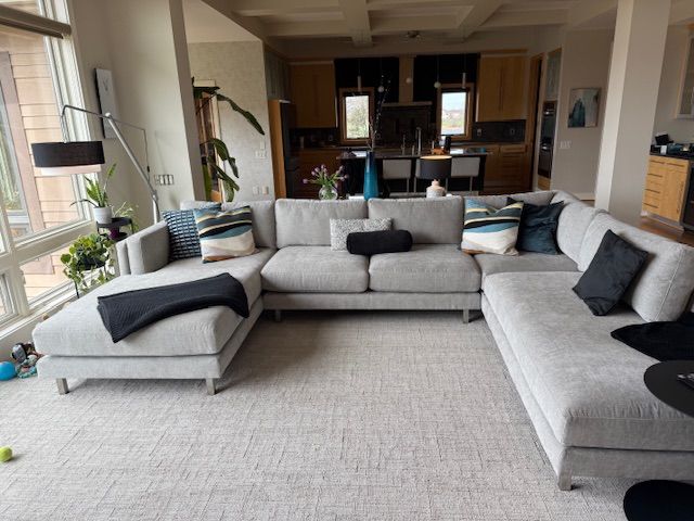 Spacious living room with a gray sectional sofa, black pillows, and a view into the kitchen.
