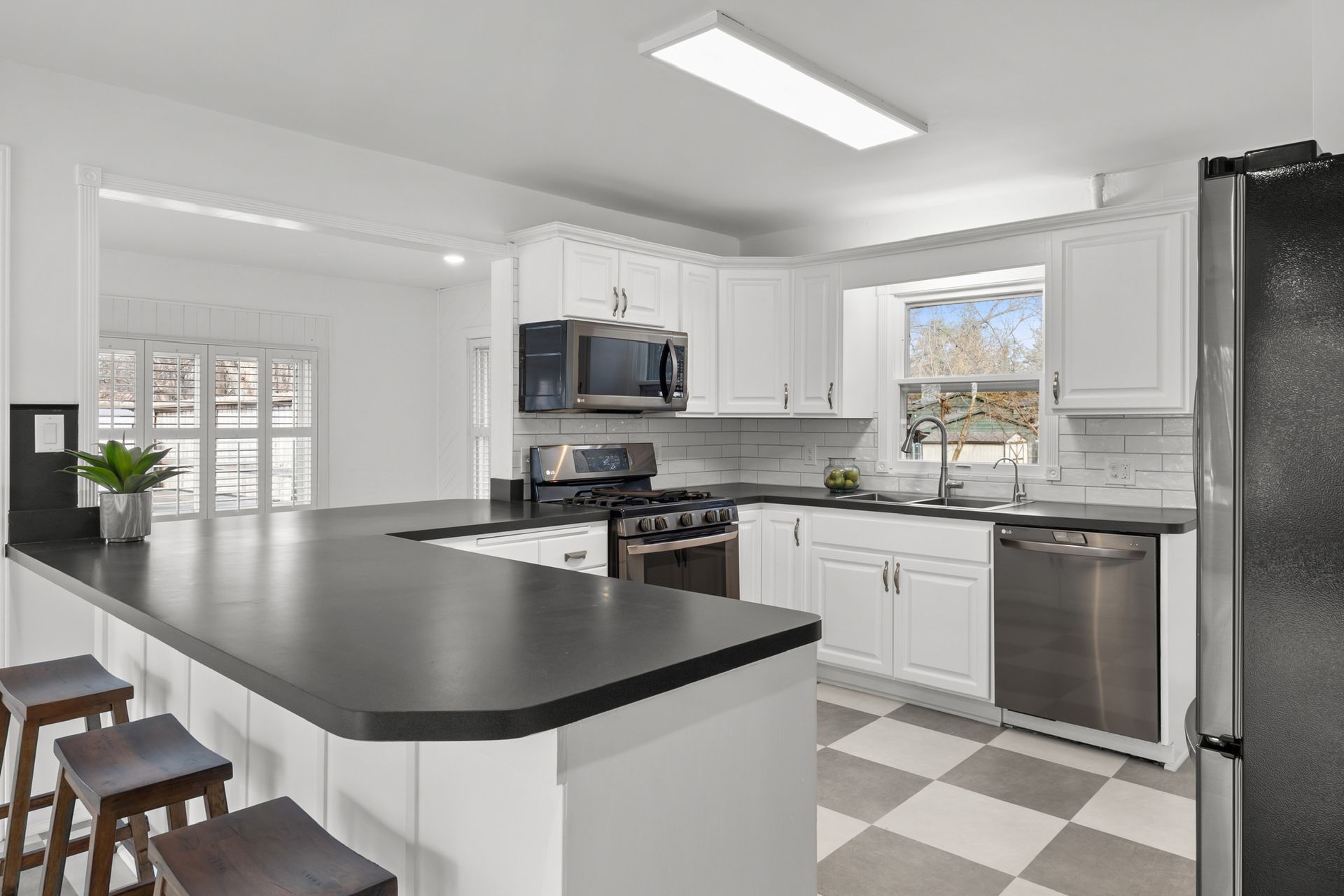 Modern white kitchen with black countertops, stainless steel appliances, and checkered tile floor