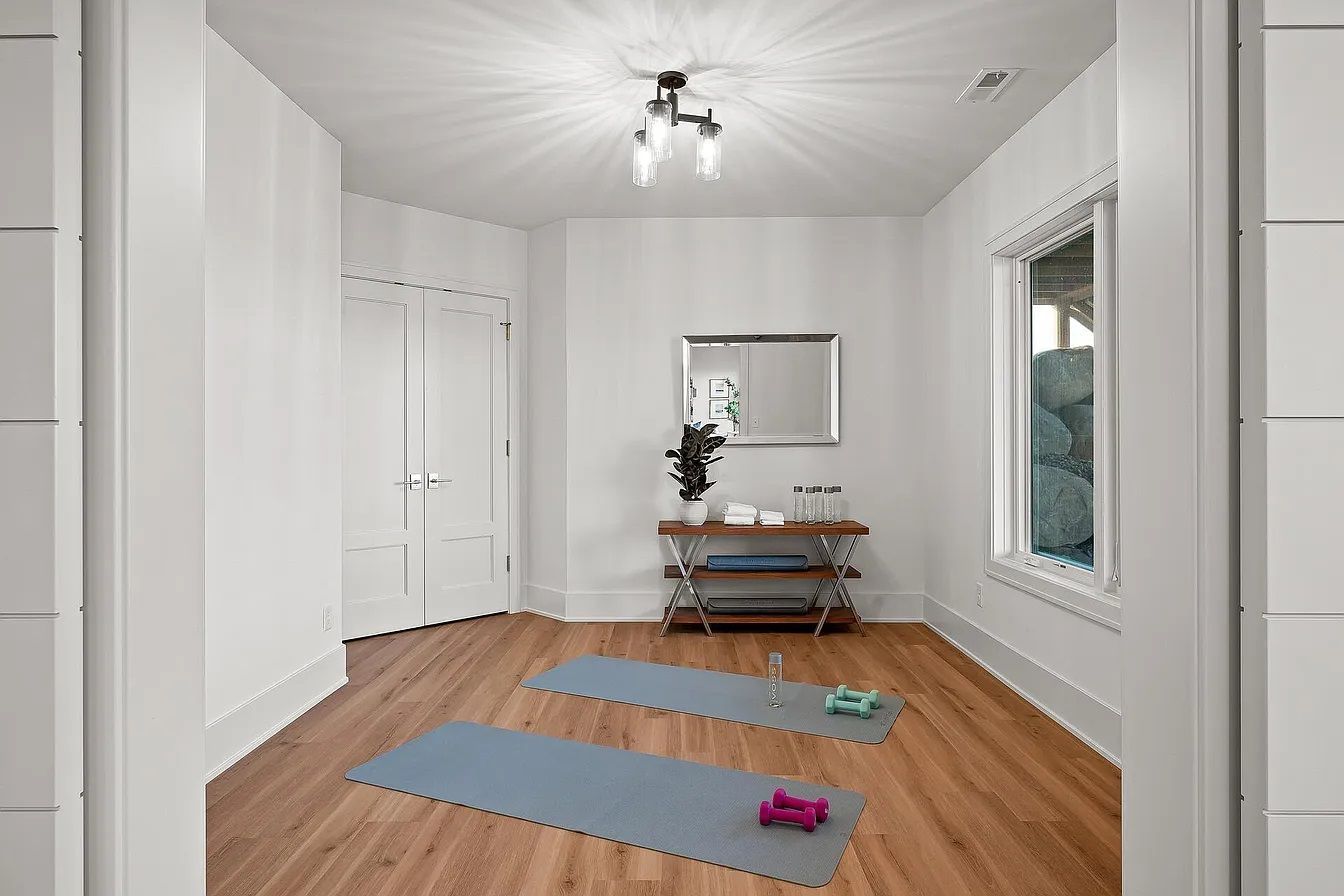 Bright hallway with wood floor, white walls, two yoga mats, and a bench under a mirror.