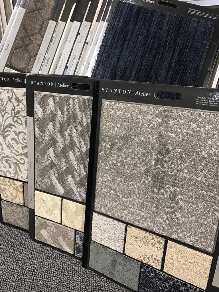 Display of patterned carpet tiles in black frames, showing gray, beige, and dark blue samples.