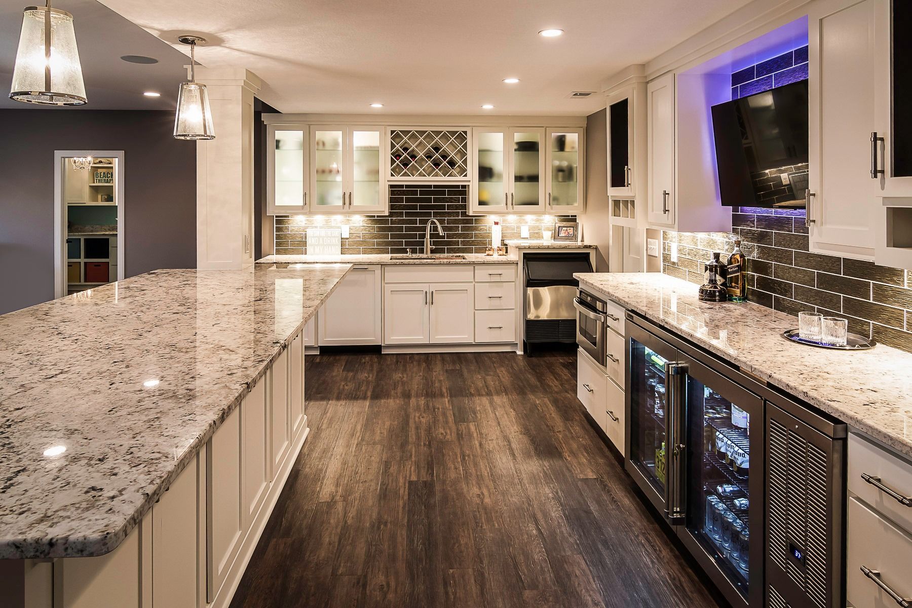 Modern kitchen with granite countertops, dark wood floors, white cabinets, and glass-front wine storage.