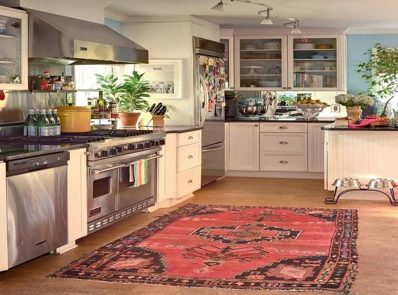 Bright kitchen with stainless steel appliances, white cabinets, potted plants, and a red patterned rug.