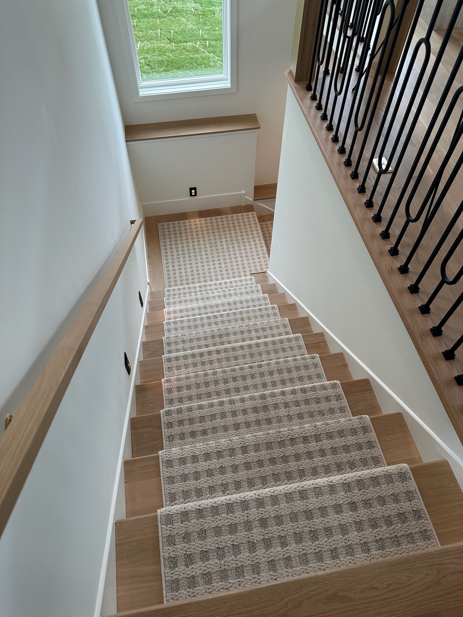 Carpeted staircase with white walls, wood railing, and window at the landing