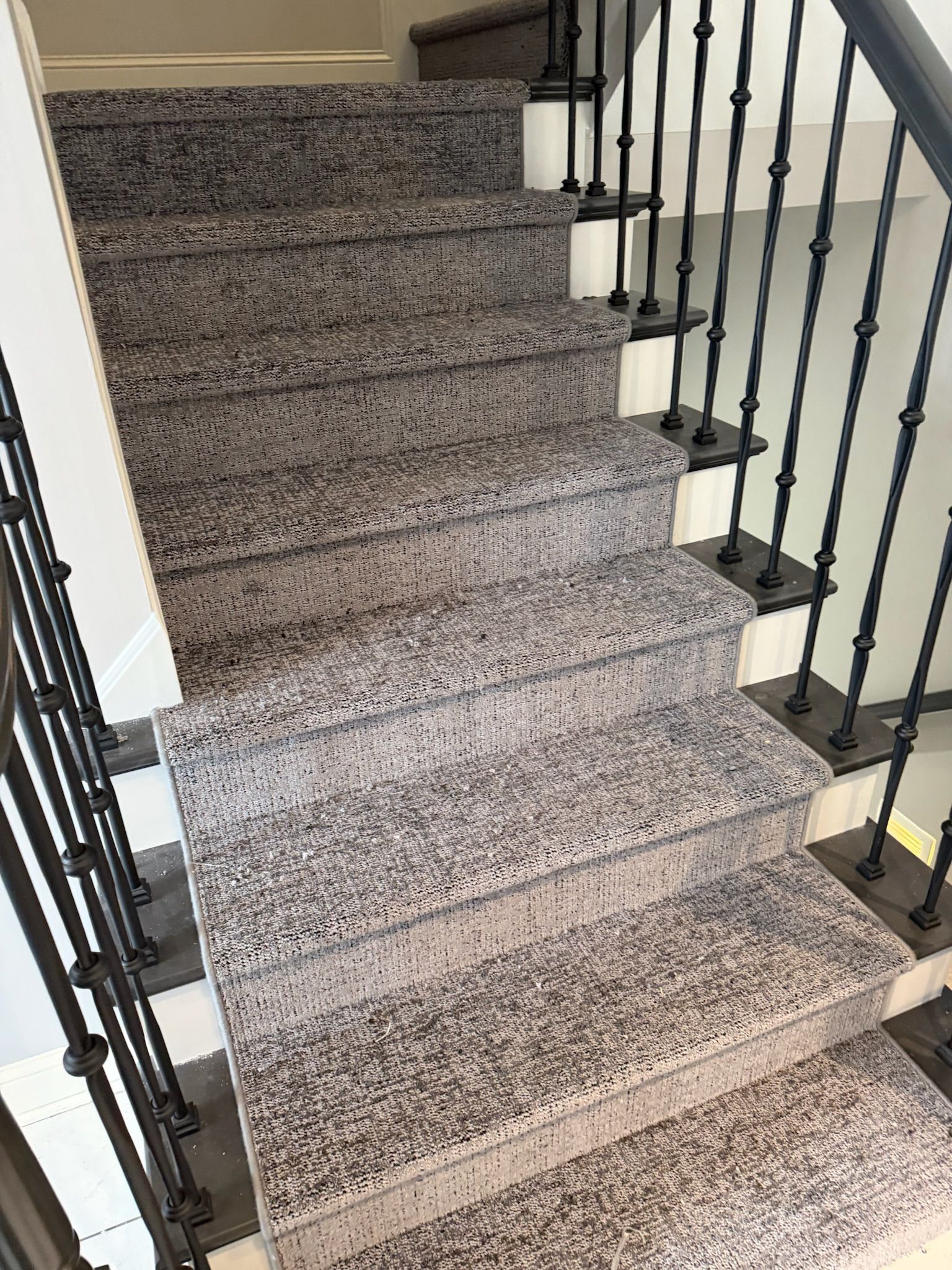 Carpeted staircase with black wrought-iron railings and white walls indoors