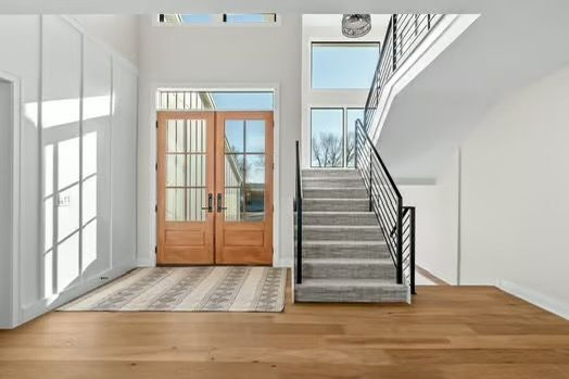 Bright entryway with wooden doors, staircase, and hardwood floor in a modern home