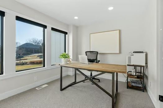 Bright home office with a wooden desk, black chair, wall art, and large windows overlooking hills