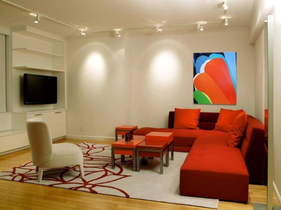 Modern living room with orange sectional sofa, white chair, wall TV, and abstract art on a cream wall.