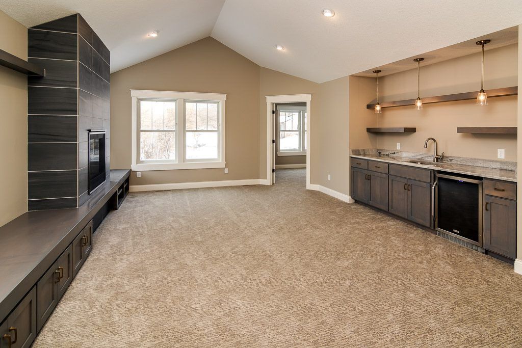 Spacious beige living room with carpet, windows, built-in shelving, and a kitchen bar on the right