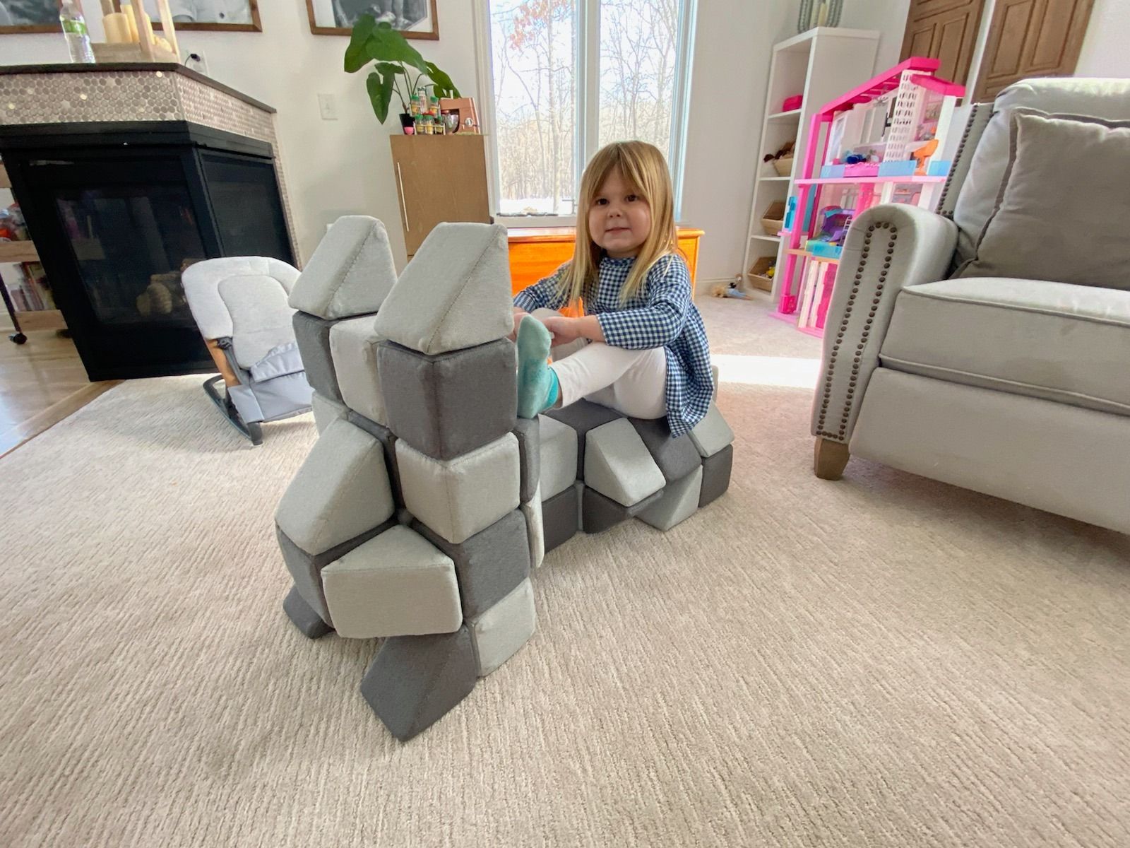 Child playing with a gray foam block fort in a living room
