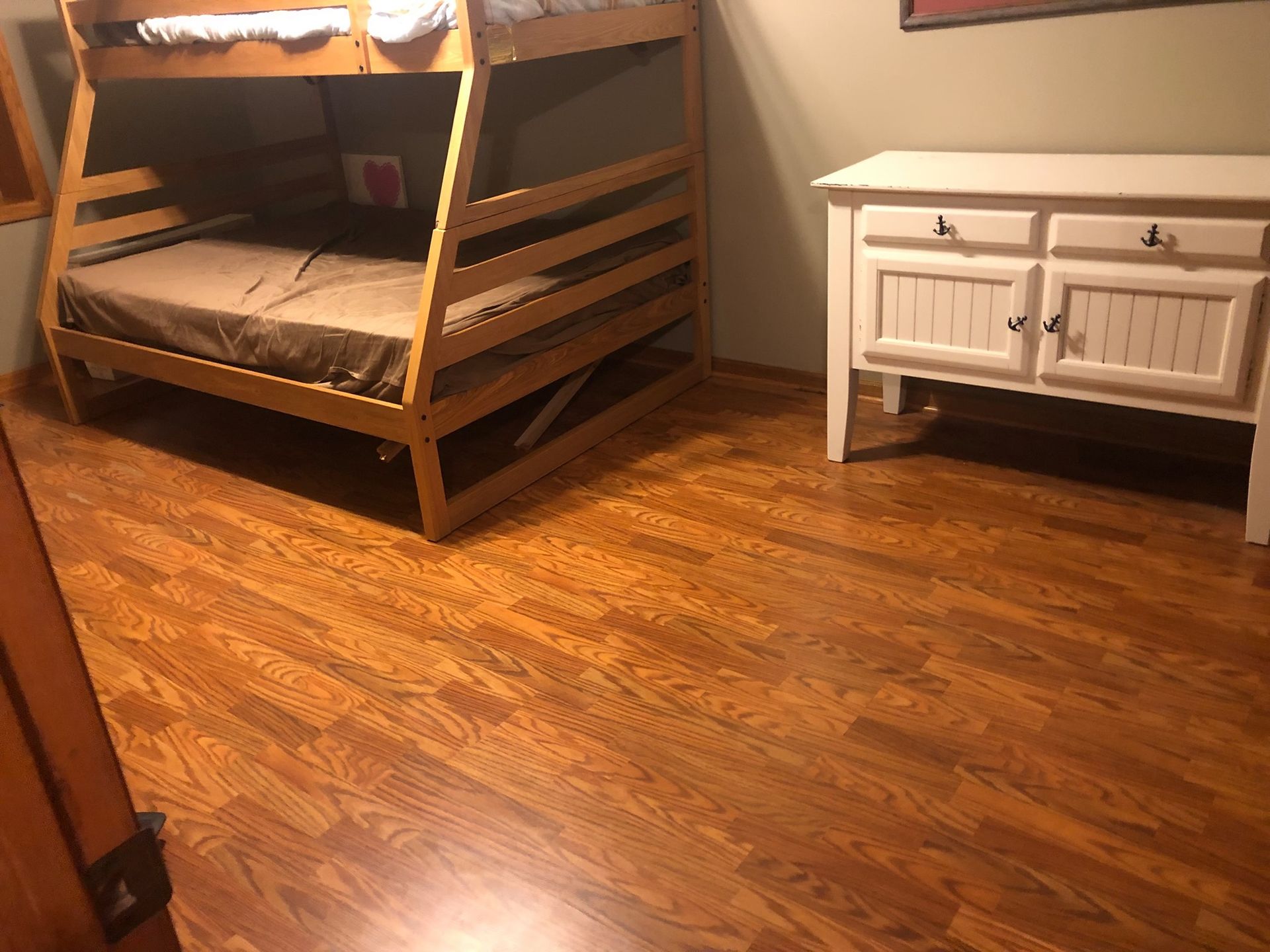 Wooden bunk bed and white dresser in a warmly lit bedroom with hardwood floors