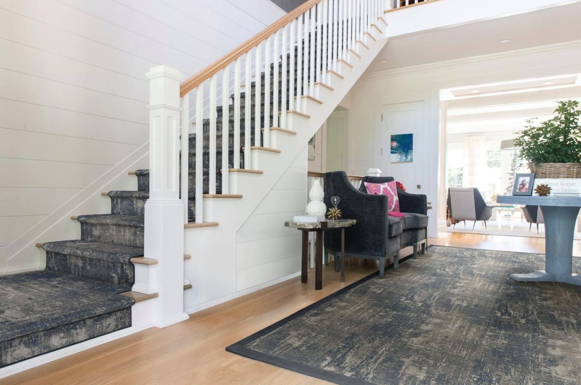 Bright entryway with staircase, gray carpet, white walls, and a console table near a seating area.