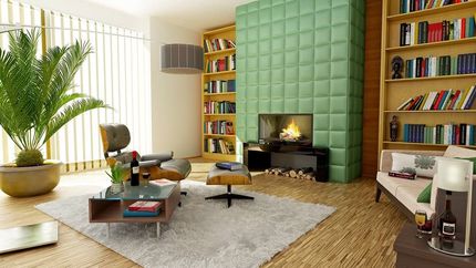 Modern living room with green tiled fireplace, bookshelves, beige sofa, and large potted plant by the window
