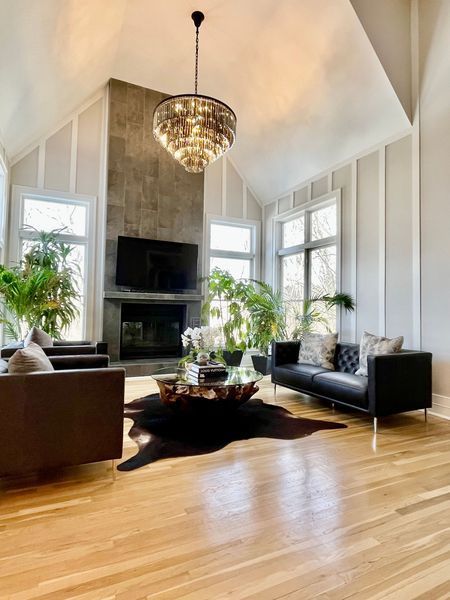 living room is lit up by natural light with a gold chandelier and a glass table over an animal rug