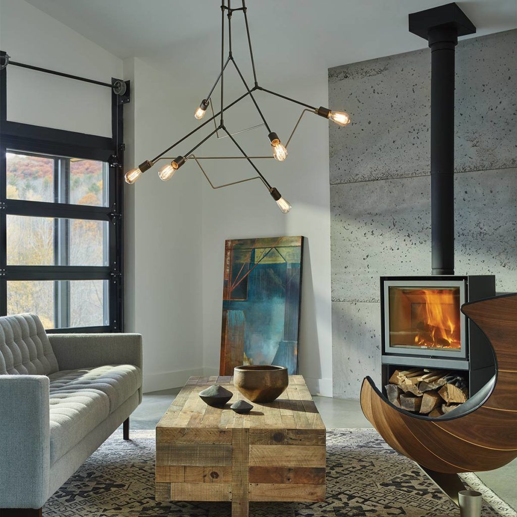 Modern living room with a gray sofa, rustic wooden coffee table, industrial chandelier, and a fireplace against a wall.