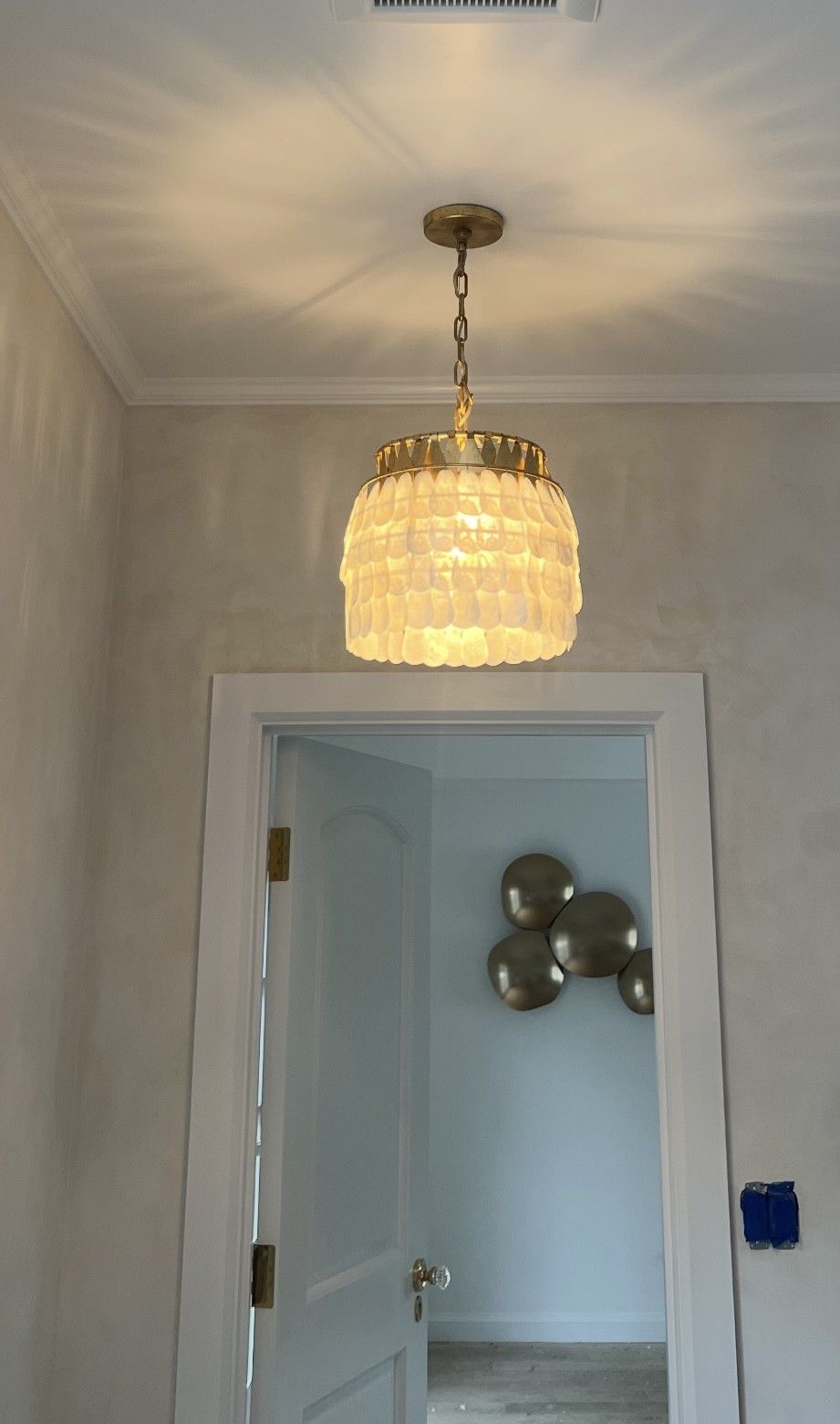 Hallway with a crystal chandelier casting light on the ceiling, open doorway, and silver balloon-like decor beyond