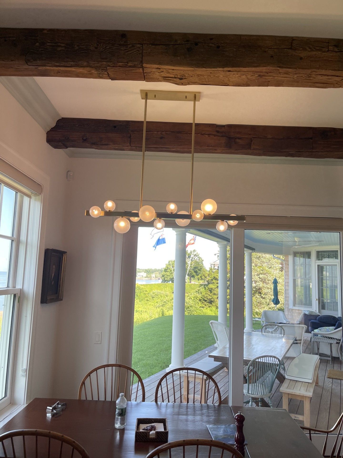 Dining room with rustic beams, pendant light, wooden table, and open view to a sunlit patio and garden.
