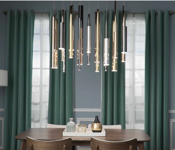 A dining room featuring a modern multi-pendant light fixture hanging above a wooden table with teal curtains in the back.