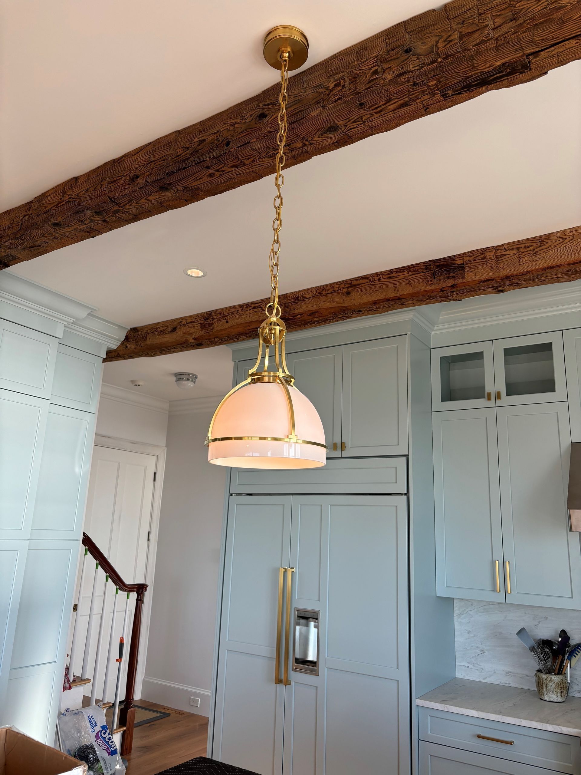Gold pendant lamp in a light blue kitchen with wood beams.