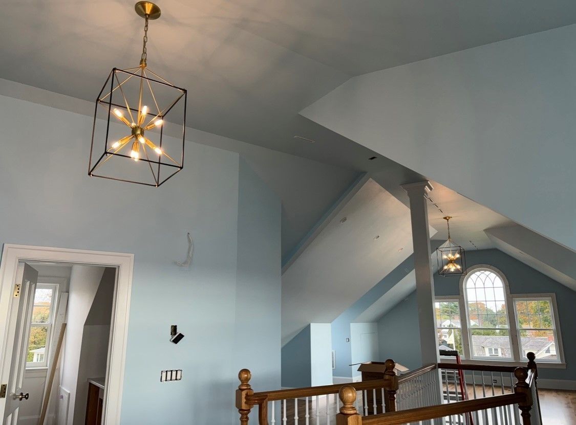Interior view of a two-story room with light blue walls, a gold and black light fixture, and a staircase.