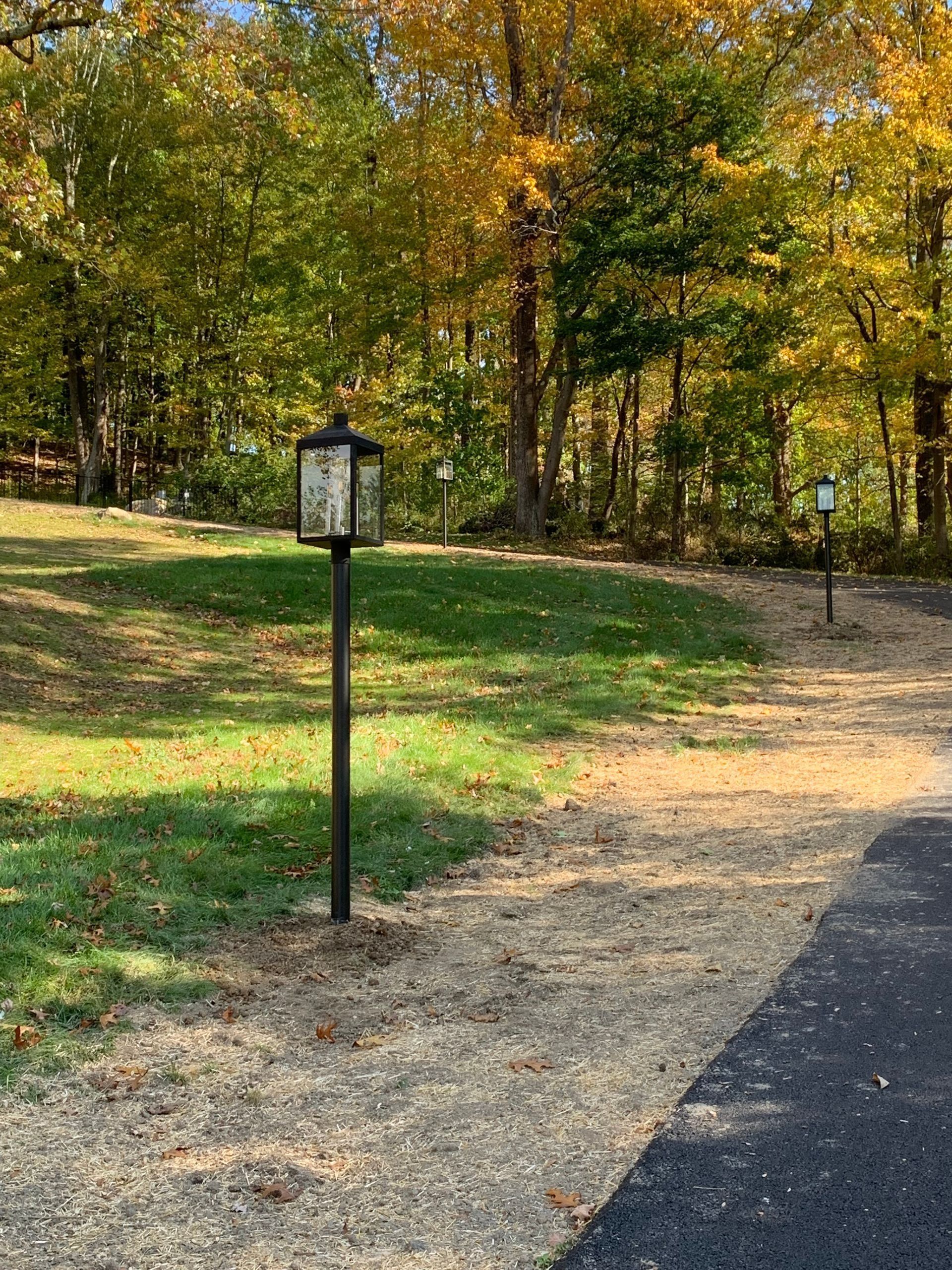 Gravel path through a grassy area, with trees in the background. A black lamp post stands in the foreground.