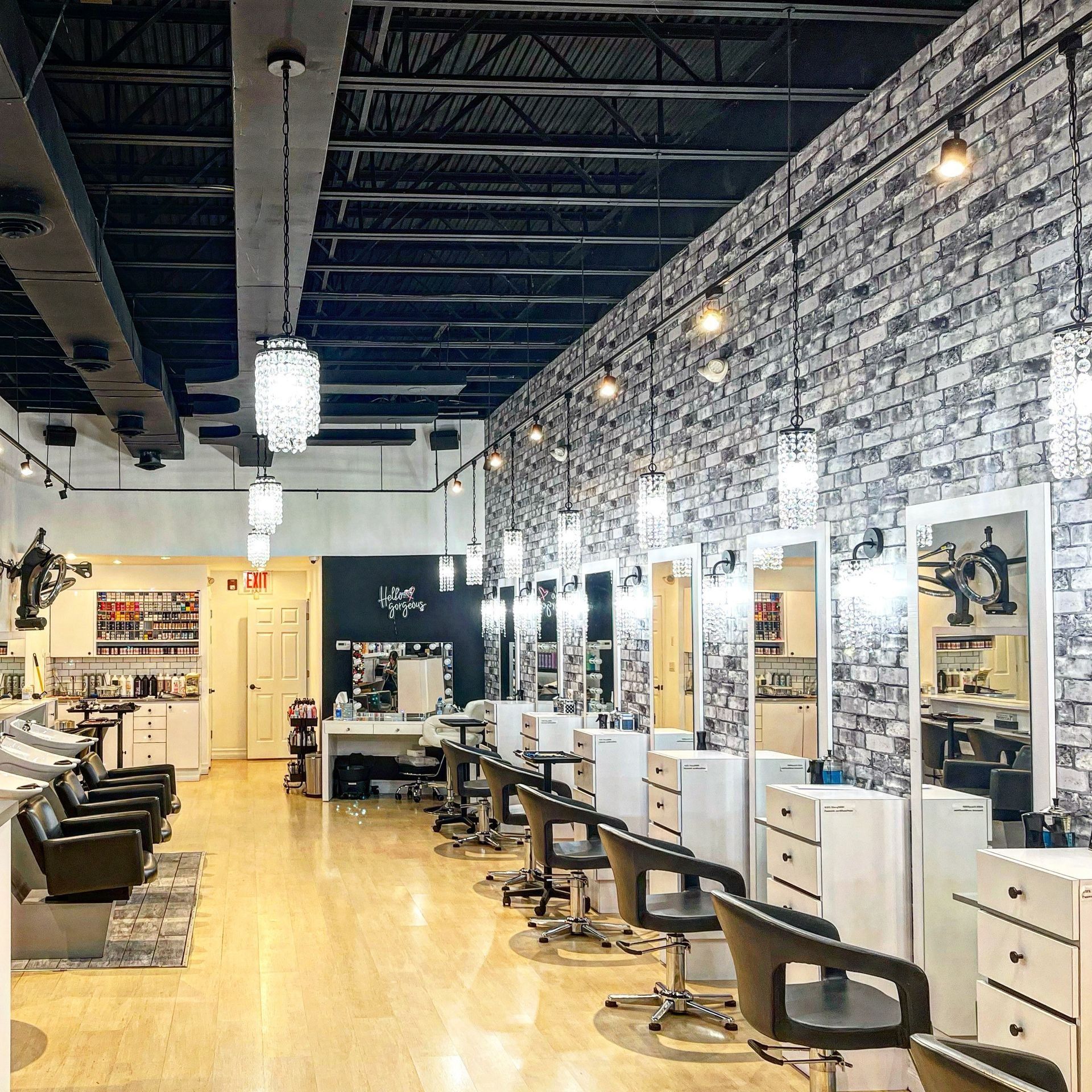 Interior of a hair salon with styling stations, mirrors, and brick-patterned wallpaper.