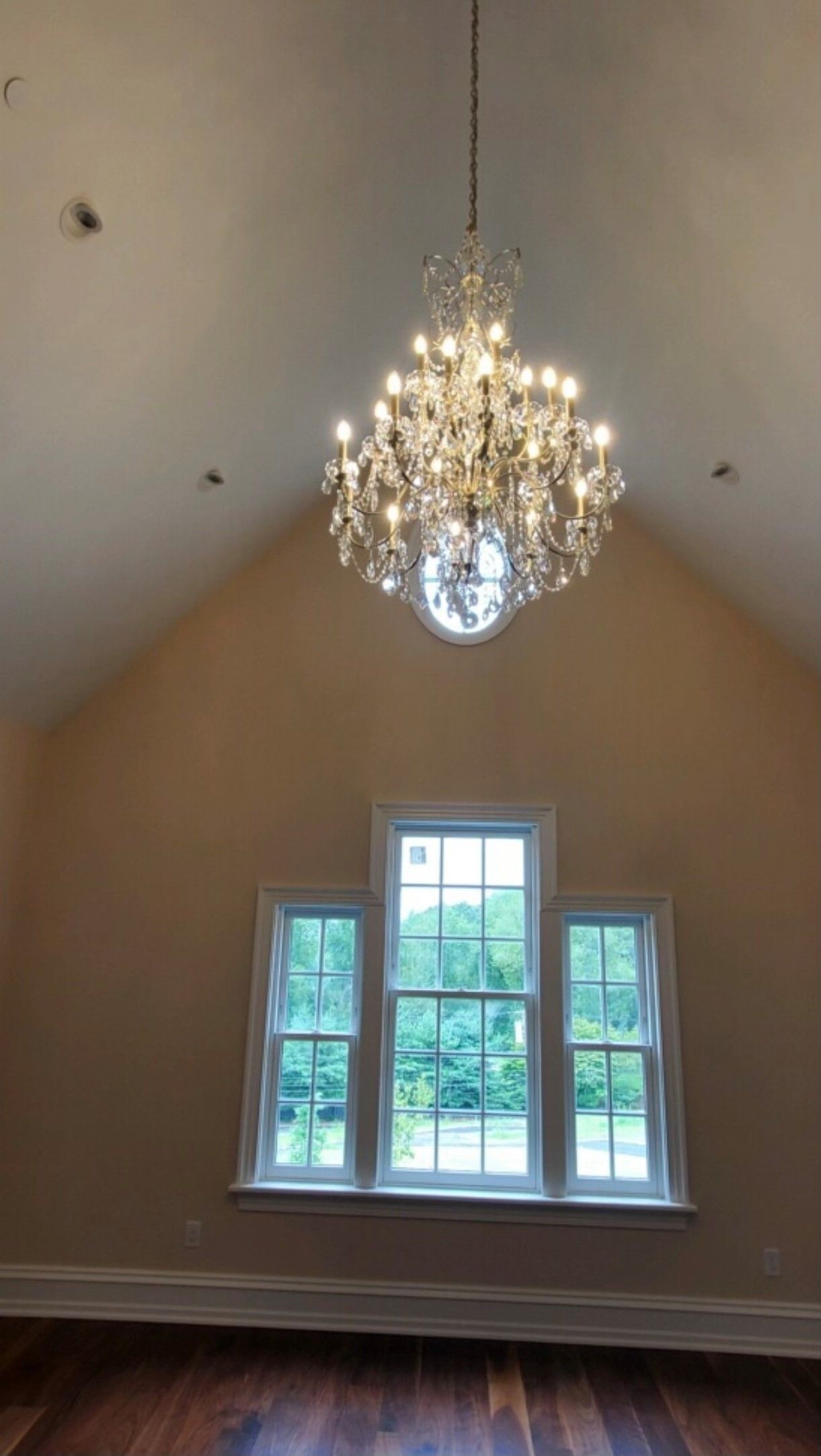 Chandelier hangs above a window with three panes in a room with tall, angled walls.