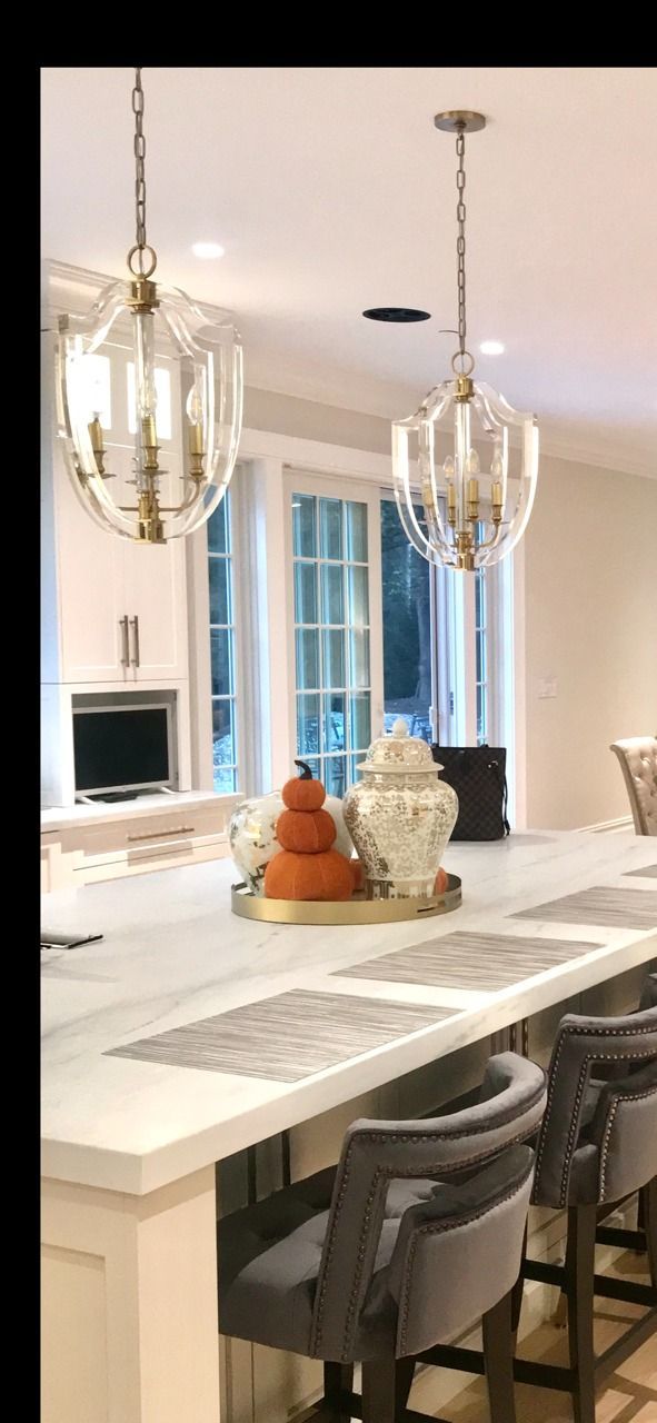 Kitchen with pendant lights, a long white countertop, and gray upholstered bar stools. Decorative pumpkins sit on the counter.