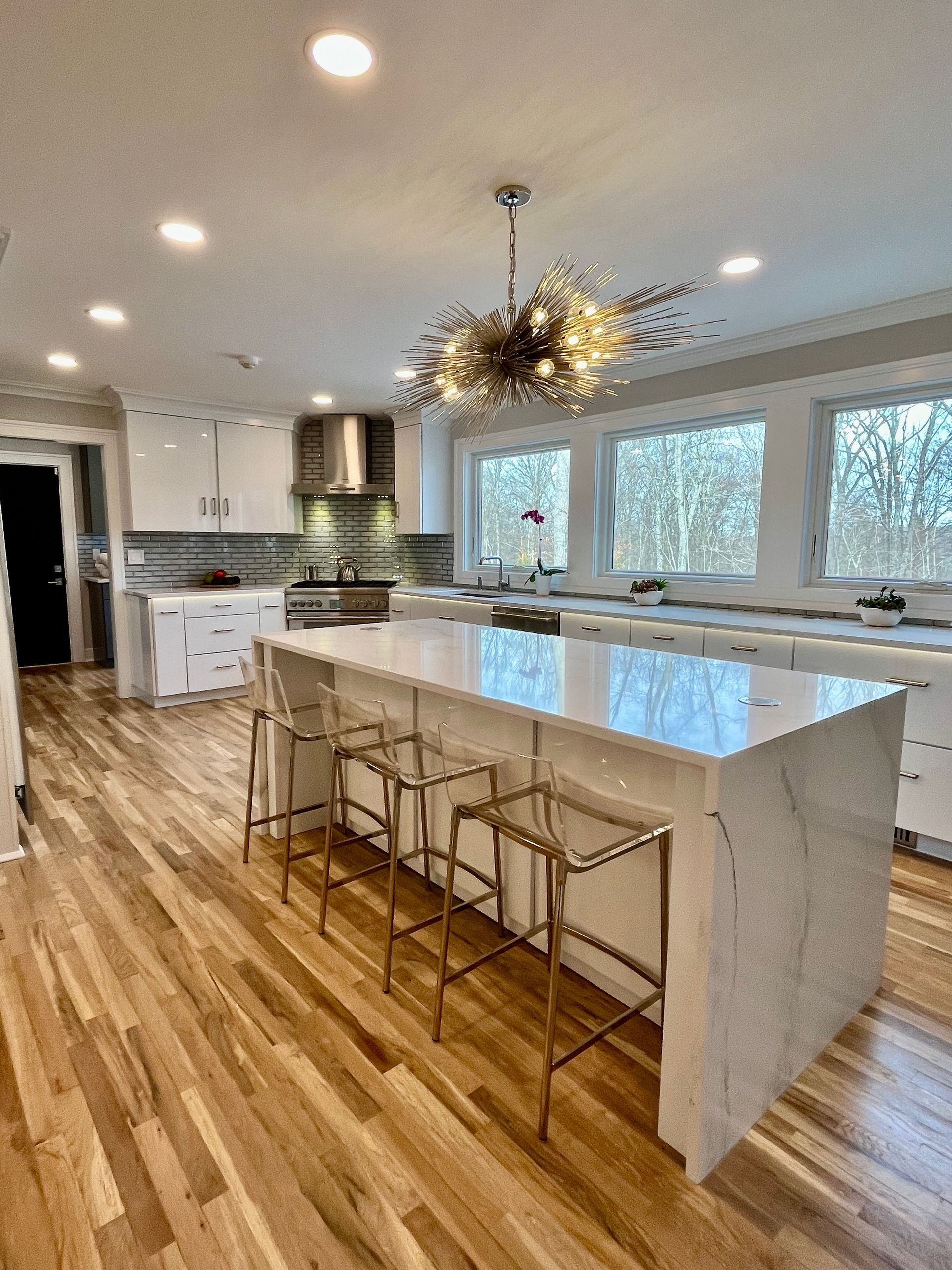 Modern kitchen with a large island, white cabinets, and wood flooring.