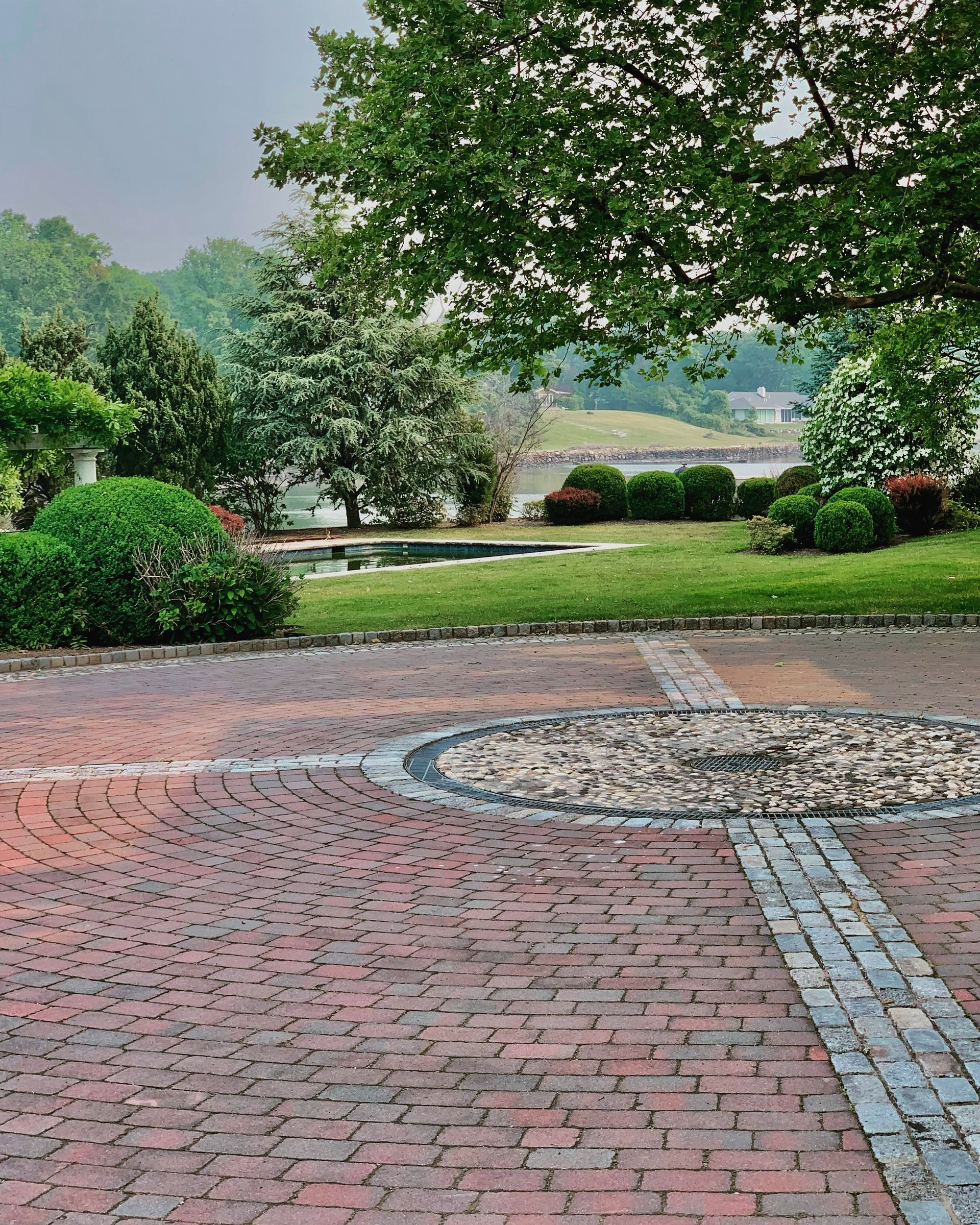 Brick patio leads to a grassy area with trees and a lake in the distance.